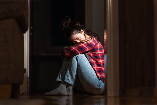 Panic disorder and obsessive-compulsive disorder. Crying young Caucasian woman sits down on floor in dark living room. Concept of psychology and mental problems