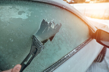 Scraping ice from the car window. Concept of vehicle preparation for a ride when the outside temperature is below zero.