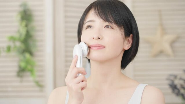 部屋で美顔器を使っている若い女性　美容イメージ	
