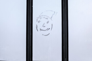 Face with a smile on the frosty glass of the balcony