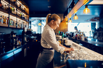 A bartender is working with clean glasses behind a counter in a bar.