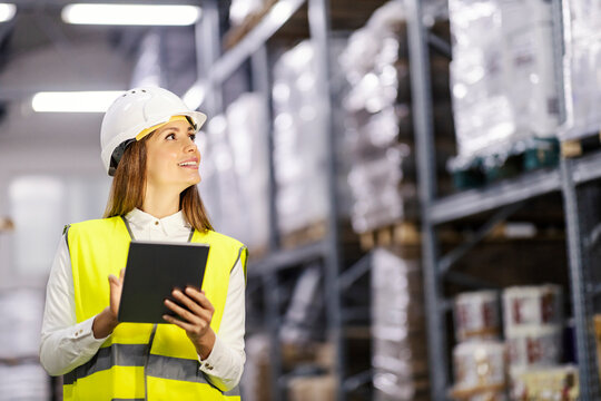 Smiling warehouse manager is dispatching with tablet while looking in shelves.