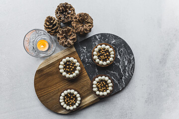 Top-down view of four chocolate mini dessert tarts on wooden and stone minimalist platter next to burning candle and pinecones. Festive desserts. Horizontal shot . High quality photo