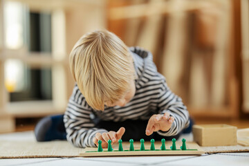A boy is arranging figures on educational wooden toy and learning through the game at montessori...