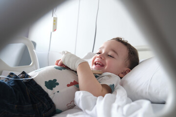 child in hospital lying in bed with mobile phone smiling