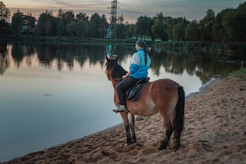 Young beautiful girl on a horse near the river in the evening.