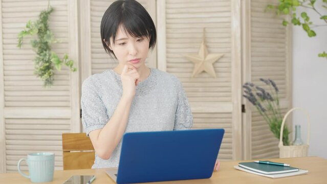 ノートパソコンの前で考え事をする若い女性
