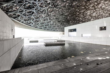 Atrium of the Louvre museum in Abu Dhabi, with latticework dome, marble walls and floor, and steps descending into the water