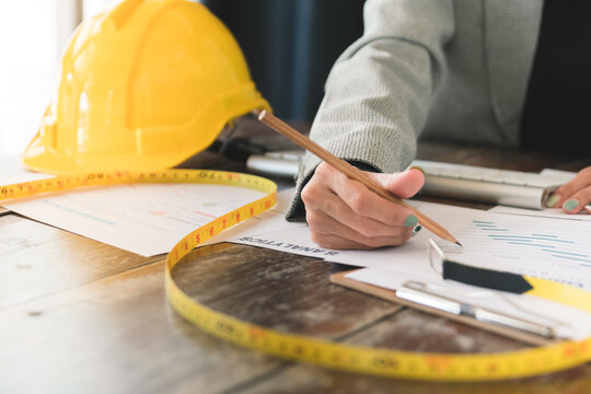Close-up of female engineer inspecting the blueprint of the building on the desk in workplace, Engineering tools and construction concept