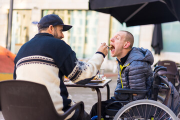 A disabled person eating with the help of a brother having fun, terrace of a restaurant