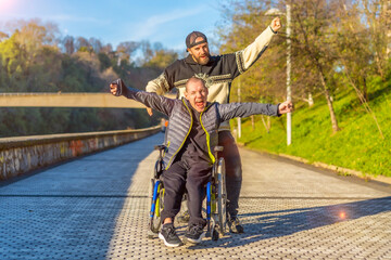 Disabled person in wheelchair with friend overjoyed, smiling, enjoying with arms up, vistoria,...