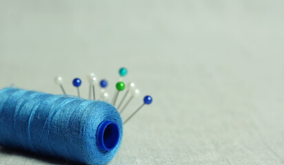 Spool of blue thread and tailor's needles. Accessories for sewing on a light background.
