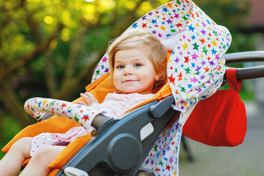 Portrait of little cute smiling toddler girl sitting in stroller or pram and going for a walk. Happy cute baby child having fun outdoors. Healthy daughter.