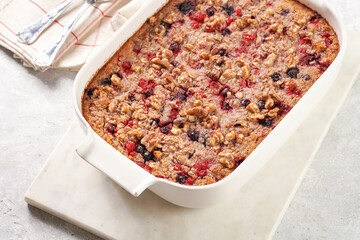 breakfast casserole idea - oven berry baked oatmeal with almonds, walnuts and coconut flakes in a white porcelain baking form on a marble board, top view