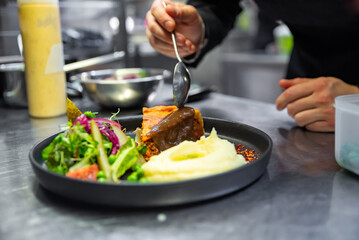 chef hand preparing Meat Pie with mashed potato and salad on restaurant kitchen