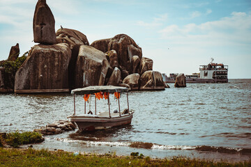 23.04.2022 - Mwanza, Tanzania - Boat floating on beach shore next to huge rocks on a sunny day in...