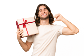 Young handsome man holding a gift over isolated background proud and self-satisfied