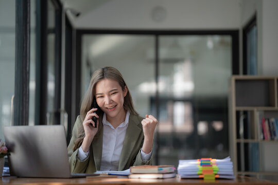 Successful Confident Beautiful Asian Businesswoman, Business Leader, And Manager Working At The Office, Talking On The Phone With Friends Or Colleagues, Looking Away, Smiling