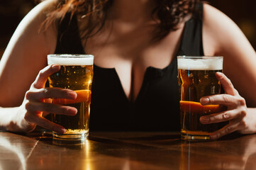 two glasses of light foam beer lager in hands of a woman with big sexy breasts at bar in pub