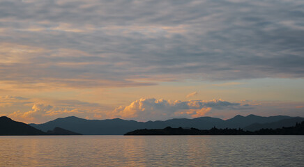 Gorgeous sunset sky with clouds over the sea. Silhouettes of a range of islands and mountains on the horizon. Idea for backgrounds or screens. Dramatic sunset, beauty of nature, vacation time