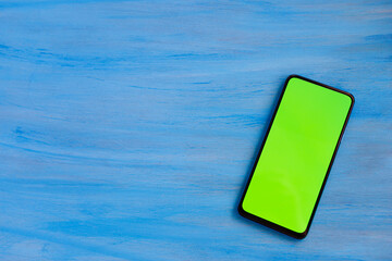 Phone smartphone, green screen on Blue wood background top view