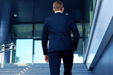 Stylish successful businessman goes up the stairs of the office building.