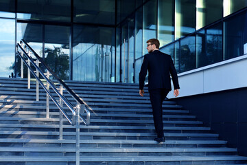 Stylish successful businessman goes up the stairs of the office building.
