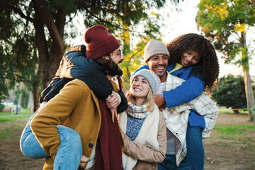Five millennial friends have fun piggybacking at park outdoor. Group of multiethnic young people smiling and carrying his girlfriends, enjoying a weekend trip. Lifestyle concept. High quality photo