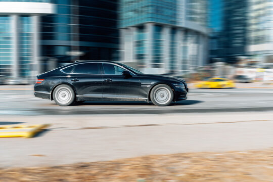 Luxury business car Genesis G80 cruising the streets. Motion image of black shiny car driving on the city road