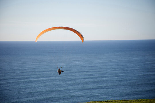 Male paraglider rides over the ocean close to the paragliding port in Torrey Pines, San Diego, California.