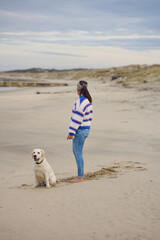 Middle-aged brunette woman on the empty beach with her labrador retriever dog
