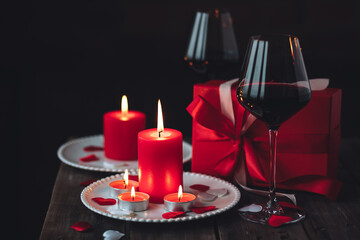 Saint Valentine's Day celebration. Red burning candles, hearts, gift box, postcard on dark wooden background. Happy holiday . Table decor for festive dinner, romantic atmosphere. Copy space for text