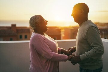 Senior african couple dancing outdoors with sunset on background - Love and joyful elderly lifestyle concept 