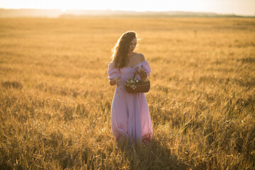 a girl with long dark hair in a lilac dress with a basket in her hands at sunset in a wheat field