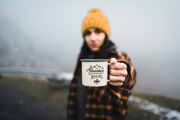 Young woman climber holding outdoor coffee mug or cup with popular adventure begins text. Morning...