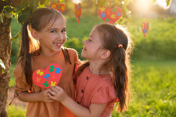 Two cute funny happy loving girls hold a heart-shaped card with colored puzzles supporting each...