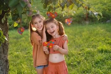 Two funny little girls are laughing standing by decorated tree with cards with puzzles in garden...