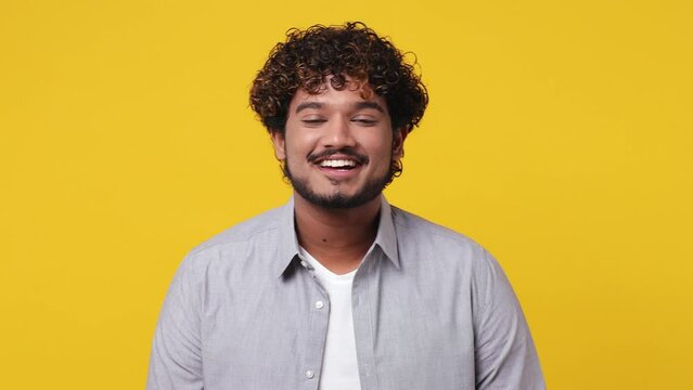 Young smiling happy fun cheerful satisfied optimist positive cool Indian man 20s wearing casual grey shirt looking camera isolated on plain yellow background studio portrait. People lifestyle concept