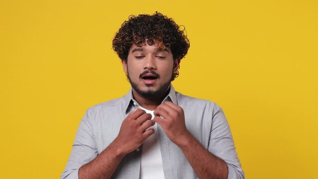 Young scared shocked sad Indian man 20s wears casual grey shirt look camera covering hiding face with hands peep through fingers isolated on plain yellow background studio. People lifestyle concept