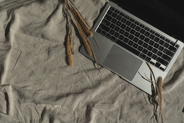 Laptop computer, dried grass on neutral crumpled linen cloth. Top view minimalist aesthetic luxury bohemian workspace. Flatlay