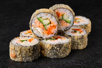 baked sushi rolls with salmon, cucumber and flying fish roe on black concrete background.