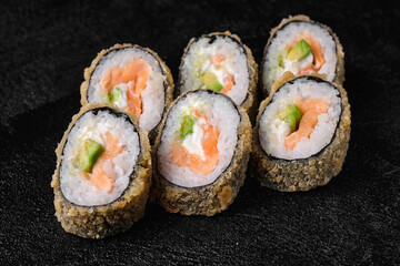 baked sushi rolls with salmon and avocado on black concrete background