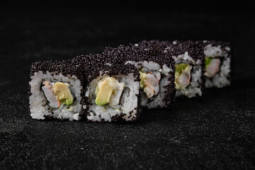 Sushi roll with shrimp inside and black flying fish roe on top on black background