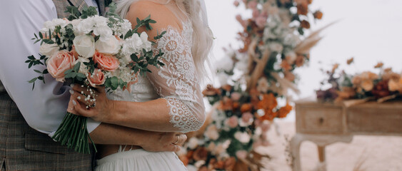 Close up of newly wife and husband hugging outdoors and holding beautiful bouquet.