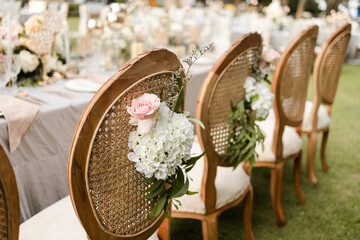Wedding wooden chairs decorated with flowers. Rattan chairs standing by reception dinner table....