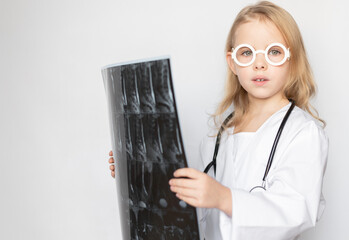 Caucasian child, little doctor looking serious at camera, holding x-ray film, standing on neutral background