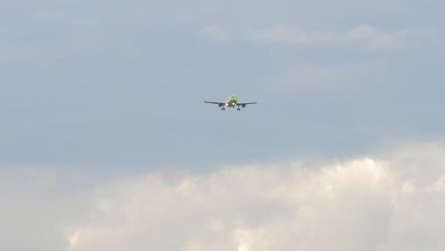 Passenger plane with green livery approaching to land in a cloudy sky, front view