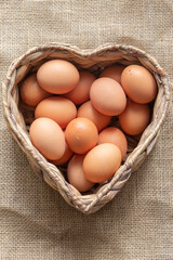 Free range chicken eggs in a heart shaped water hyacinth wicker basket. On a hessian sack cloth background