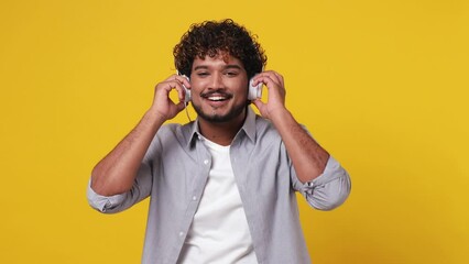 Vivid cheerful young Indian man wear casual grey shirt listen mp3 music in headphones dance sing song fooling around have fun enjoy relax isolated on plain yellow background. People lifestyle concept