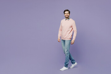 Full body sideways happy fun young caucasian IT man he wears casual clothes pink sweater glasses walking going strolling look camera isolated on plain pastel light purple background studio portrait.